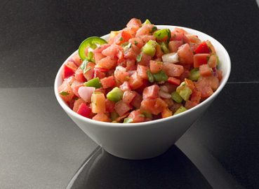 Tilted white bowl of fresh cut pico de gallo on a dark background